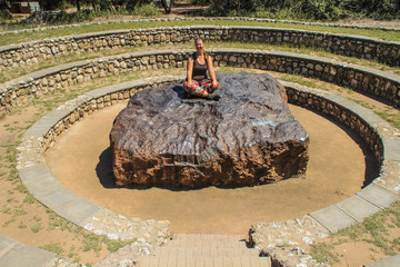 The largest meteorite in the world at Grootfontein, Namibia. A huge piece of iron from space. White girl tourist sitting on a meteorite