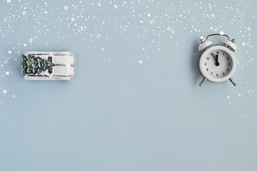 A cozy winter card with a Christmas car and a small alarm clock under the snow on a blue mint background.