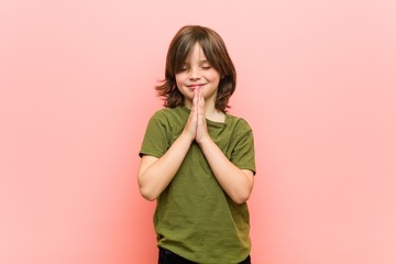 Little boy holding hands in pray near mouth, feels confident.