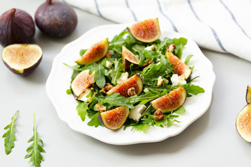 Salad with arugula, figs, cheese, walnut and honey. Autumn salad with figs and cheese on a white plate.