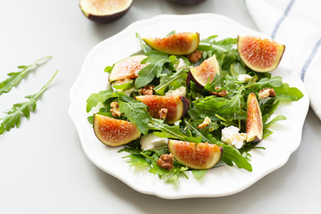 Salad with arugula, figs, cheese, walnut and honey. Autumn salad with figs and cheese on a white plate.