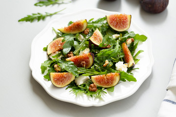 Salad with arugula, figs, cheese, walnut and honey. Autumn salad with figs and cheese on a white plate.