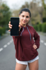 Sporty young woman showing smartphone. Focus on phone screen. Fitness workout app concept.