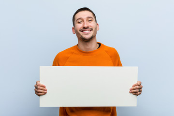 Young caucasian man holding a placard happy, smiling and cheerful.