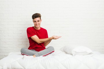 Young teenager student man on the bed holding a copy space on a palm.