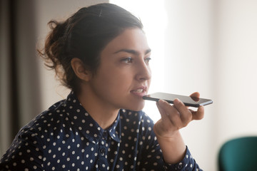 Serious young indian businesswoman holding phone talking with digital assistant