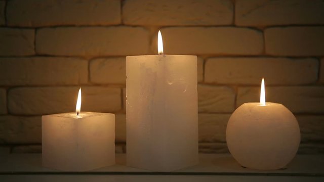 Large thick candles burn and go out from the wind. Burning candles against a light brick wall.