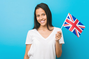 Young hispanic woman holding a united kingdom flag happy, smiling and cheerful.