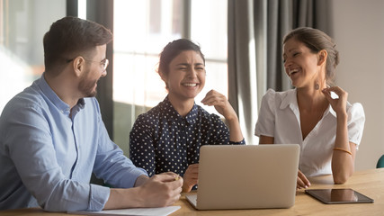 Three happy diverse coworkers talking laughing working together with laptop