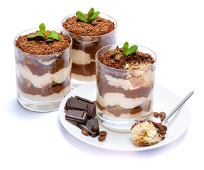 Classic tiramisu dessert in a glass cup on the plate and pieces of chocolate on white background with clipping path