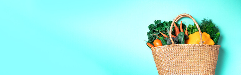 Straw basket with organic vegetables over trendy green background. Healthy food, vegetarian diet....