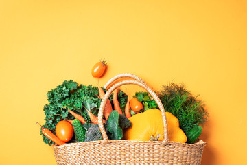 Straw basket with organic vegetables over trendy yellow background. Healthy food, vegetarian diet....