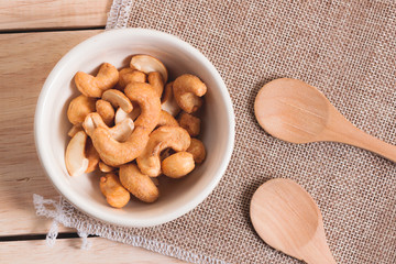 Snack on the table salted Cashew Nuts in the bowl put on sack and wood background with woodden spoon 