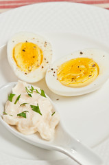 Top view, close up of a halved, hard boiled egg with firm yolk, with fresh cracked pepper, and a porcelain spoon , filled with mayonnaise and chopped parsley on a round, white plate