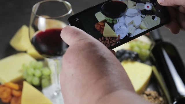 the smartphone shoots video of assorted cheeses, soft, hard, rennet and brine, fruits on the table and nuts