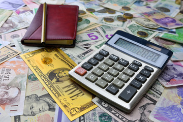 Calculator, notebook and pencil on the background of different country currency notes and one symbolic gold dollar banknote.  Financial planning concept.