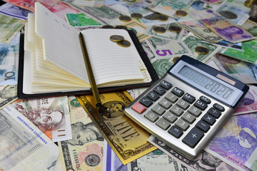 Calculator, notebook and pencil on the background of different country currency notes and one symbolic gold dollar banknote.  Financial planning concept.