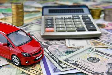 Calculator and red toy car on a variety of national currency banknotes background.  Concept of the cost of purchasing, renting and maintaining a car.