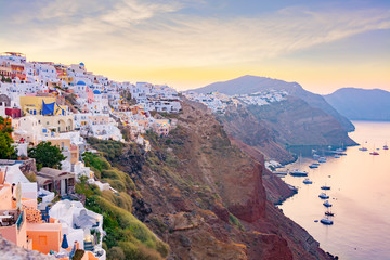 Picturesque cityscape of Oia village on Santorini Island with traditional white architecture over the Caldera mountains in Aegean sea at sunset,  Greece. Scenic travel background.
