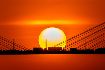 Sunset over the cable-stayed bridge with silhouette of car crossing the sea bay