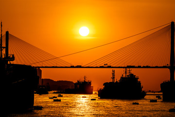 Sunset over the cable-stayed bridge with silhouette of car crossing the sea bay