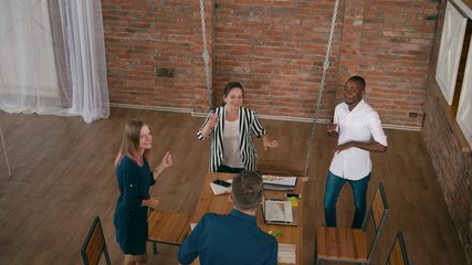 Top View Happy Casual Diverse Team is Dancing and Celebrating Business Success in Startup Loft Office. Overhead 4K Gimbal Orbit Medium Corporate Shot in Slow Motion