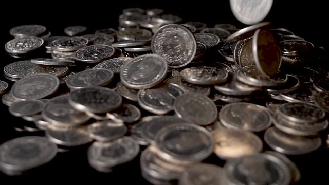 Slow motion shot of Swiss coins falling on a reflecting table in front of black background