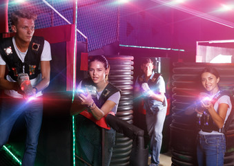 Fototapeta na wymiar Men and girl with colored laser guns playing laser tag game in