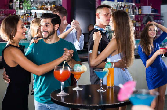 cheerful women with men are dancing in pairs in the nightclub