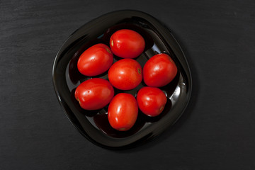 Fermented food on a black plate on an black wooden table. Pickled tomatoes and cucumbers. Salt for the winter. Traditional snack for alcohol.