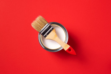 Brush and open paint can on trendy red background. Top view, copy space. Appartment renovation, repair, building and home design concept.