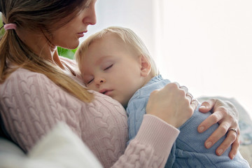 Young mother, holding her sick toddler boy, hugging him at home