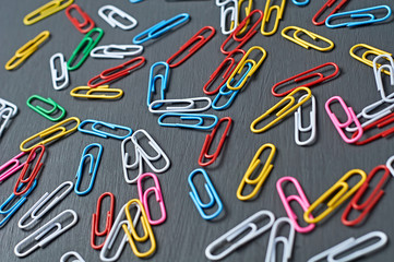 Many scattered different colors paper clips red, green, blue, yellow, white and pink for office work or education lies on dark scratched concrete table. Close-up