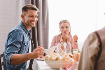 selective focus of smiling father holding gravy boat in Thanksgiving day