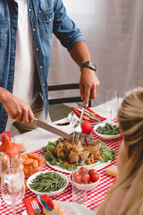 cropped view of family members sitting at table and father cutting tasty turkey in Thanksgiving day