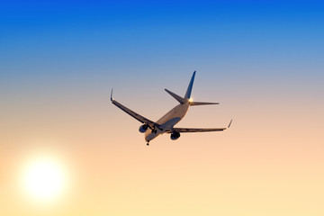 Fototapeta na wymiar Modern airplane flying against sunset sky background Passenger aircraft landing at sunrise Commercial plane taking off towards setting sun Business jet arriving with landing gear down Aerial view
