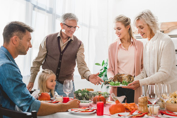  family members sitting at table and holding plate with turkey in Thanksgiving day