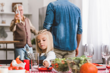 selective focus of cute kid smiling and putting on table cutlery in Thanksgiving day