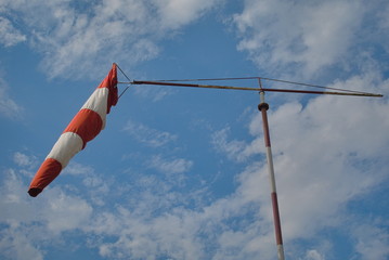 Red and white striped hood that shows the wind direction for the helicopter. Summer sky and white clouds.