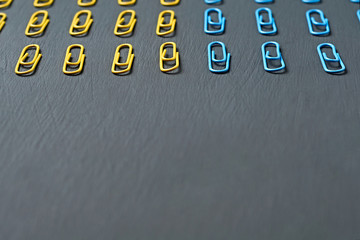 Two sections of rows of many red and yellow colors paper clips for office work or education lies on dark scratched concrete table. Space for text