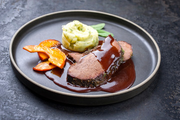 Traditional roasted beef heart with fried pumpkin slices and mashed potatoes in gravy red wine sauce as closeup on a modern design plate