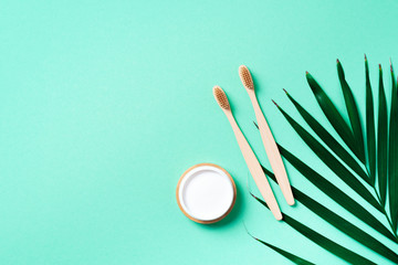 Zero waste concept. Natural toothpaste from baking soda and bamboo toothbrush on trendy green background with palm leaf. Plastic free essentials, teeth care concept. Sustainable lifestyle