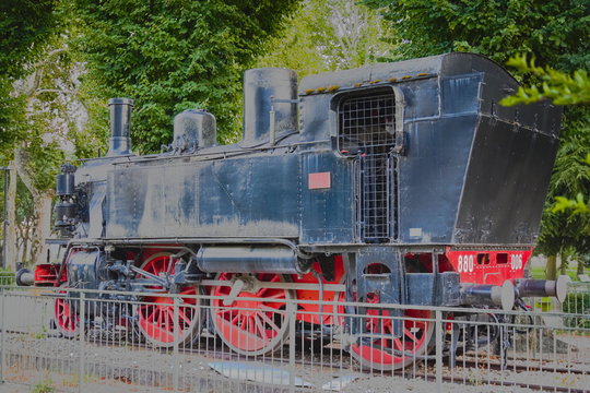 Vintage black and red steam locomotive, which stands in an open area behind the fence (in the park)