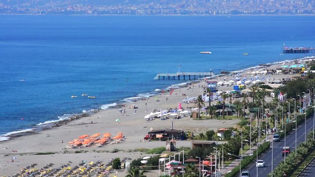Aerial view of beach in Mahmutlar Alanya on the Turkish Mediterranean Coast. Tourists and locals enjoy the beach with umbrellas and sunbeds and swim in the turquoise ocean.