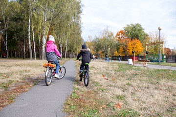 Obraz premium happy girl and boy ride bicycles in autumn park