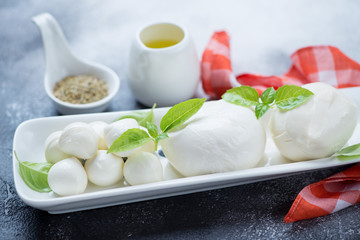Closeup of mozzarella balls of defferent sizes with olive oil and green basil leaves, selective focus