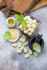 Above view of raw potato gnocchi with some cooking ingredients over beige stone background, vertical shot