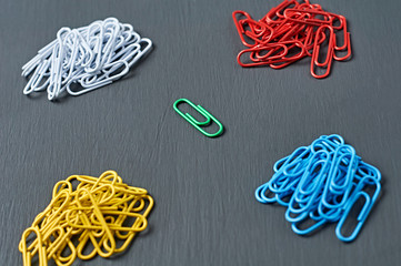 Four heaps of many paper clips for office work or education and one green color in center lies on...