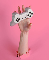 Female hand catches gamepad through torn pink paper. Minimalistic creative concept