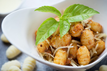 Potato gnocchi served with sun dried tomatoes pesto, parmesan and fresh green basil, close-up, selective focus